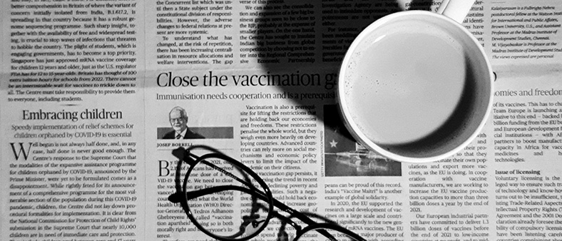 Black and white image of a newspaper with a mug and glasses on top of the newspaper